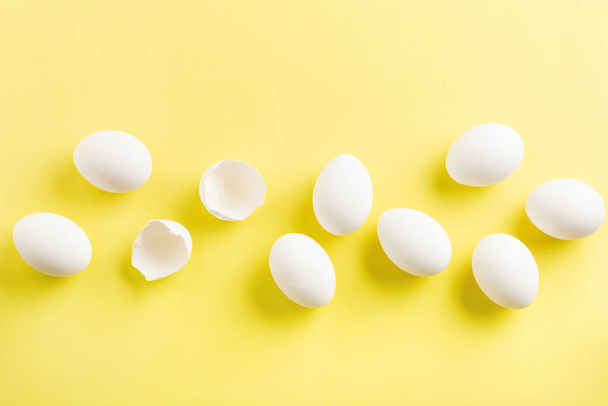 White raw chicken eggs lying in horizontal row with broken egg on yellow background. Top view. - Foto, immagini