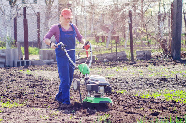 Young girl plows the land with a cultivator in spring garden. - Фото, зображення