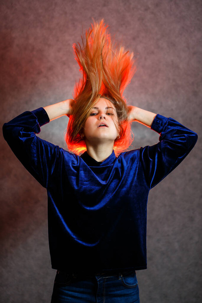 Girl with blond hair emotionally posing on a gray background. Her hair is lit in red - Fotografie, Obrázek