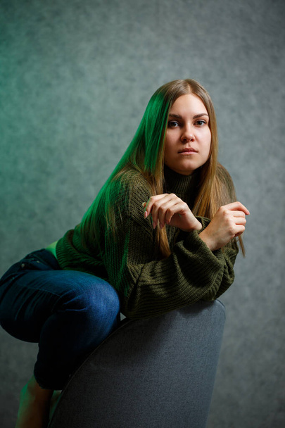Girl in a green sweater and jeans on a gray chair and smiling - Photo, image