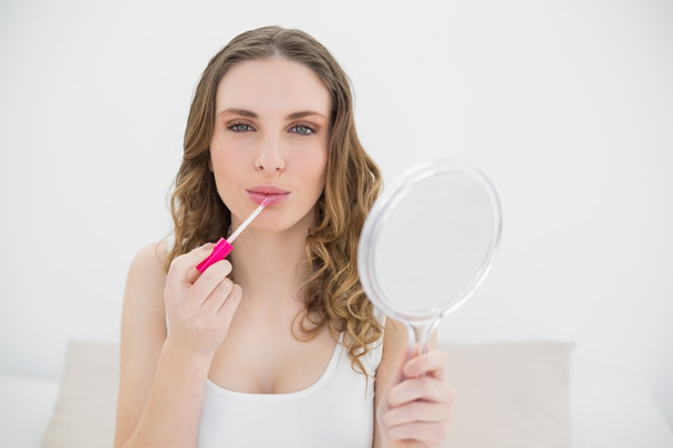 Young woman using lip gloss and looking into the camera - Photo, Image