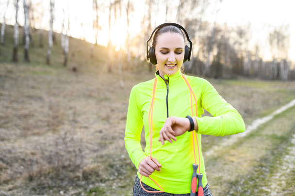 Woman looks at fitness tracker bracelet outdoors - Photo, Image