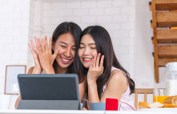 Happy asian couple lesbian getting marriage and showing ring to friend infront of tablet with video chat.LGBTQ lifestyle concept - Foto, imagen