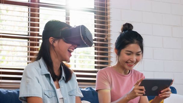 Happy asian lesbian play virtual reality goggle with tablet together at sofa in living room at cozy home - Fotoğraf, Görsel
