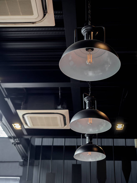 Trzy czarne okrągłe nowoczesne światła sufitowe i klimatyzator kasetowy wewnątrz kawiarni styl poddasza, w stylu pionowym. - Zdjęcie, obraz