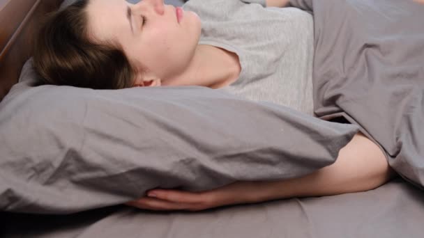 Attractive young woman sleeping well in bed hugging soft pillow, peaceful young female resting covered with blanket on grey sheets in bedroom. Teenage girl resting, good night sleep concept - Felvétel, videó