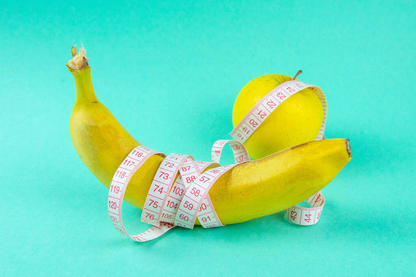 Różne rodzaje owoców, takie jak jabłka i banany, leżą na jednej nodze i owinięte są taśmą pomiarową - koncepcja zdrowego odchudzania, która sprawia, że zabawa. - Zdjęcie, obraz
