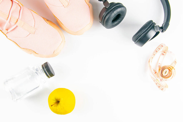 Het dieet. Pinc sneakers, hoofdtelefoon, flessen met water en appels met meetlint op een witte achtergrond. Slimming en detox-concept. - Foto, afbeelding