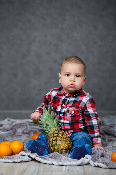 Мальчик в рубашке сидит на клетке и держит фрукты.
 - Фото, изображение