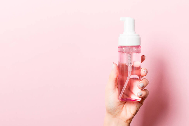 Female hand holding cosmetics spray at pink background with empty space for your design. - Foto, Imagen