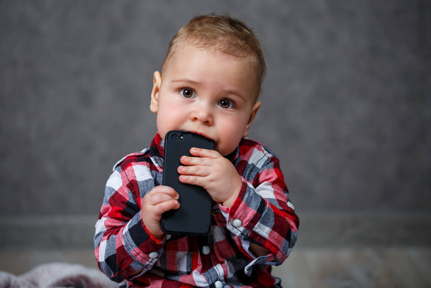 Malý chlapec v košili žvýká mobilní telefon - Fotografie, Obrázek