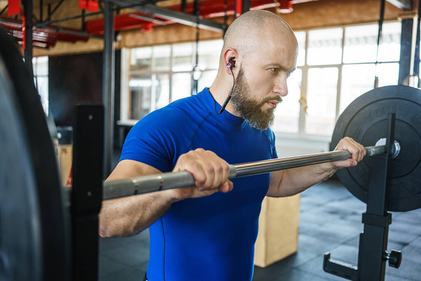 Strong bearded man at a crossfit gym lifting a barbell. - Photo, Image