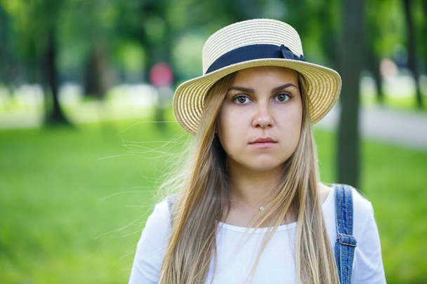 fiatal gyönyörű lány farmer overálban és egy könnyű kalap sétál a parkban - Fotó, kép