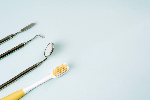 Zahnbürste und Zahnwerkzeug spiegeln sich, Haken und Pinzette auf blauem Hintergrund. Zahnpflege und Zahnarztbesuch. Kopierraum für Text. - Foto, Bild