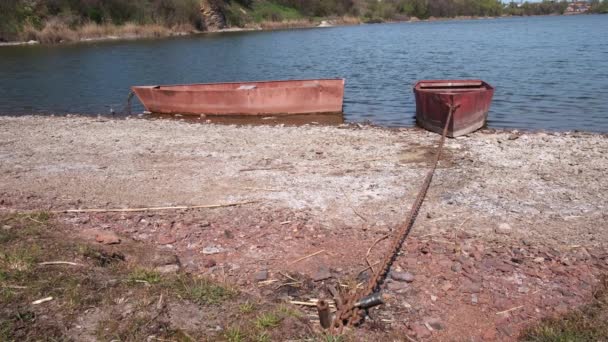 Zwei alte rostige Metallboote an einem sonnigen Tag am Ufer des Flusses angekettet - Filmmaterial, Video