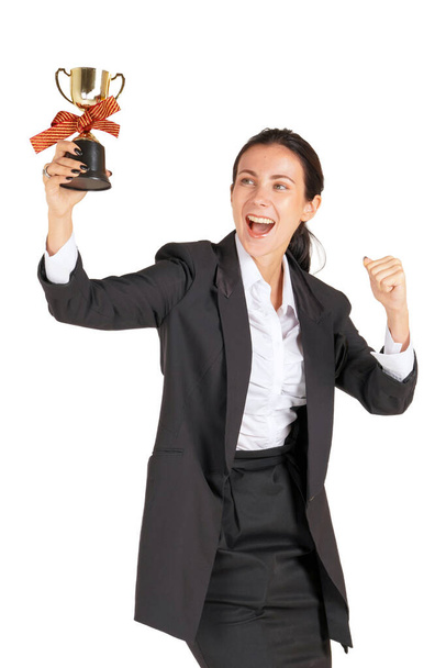 Una mujer de negocios con un traje negro con una sonrisa mirando el trofeo recibido del trabajo realizado con orgullo. Retrato sobre fondo blanco con luz de estudio
. - Foto, Imagen
