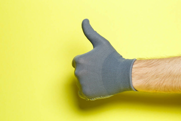 χέρι ανθρώπου, τεχνίτη, κηπουρού με γκρι γάντι σε κίτρινο φόντο - Φωτογραφία, εικόνα