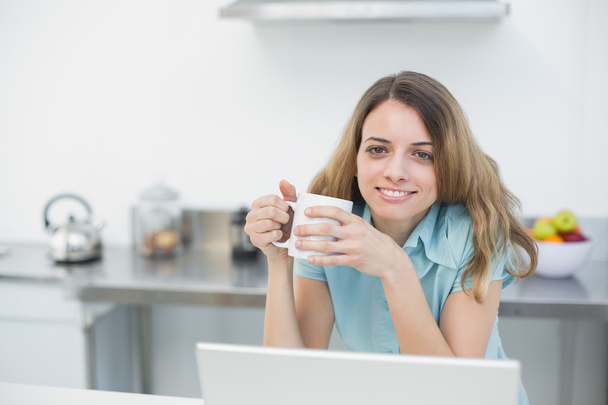 Cheerful smiling woman holding a cup posing in her kitchen - Фото, изображение