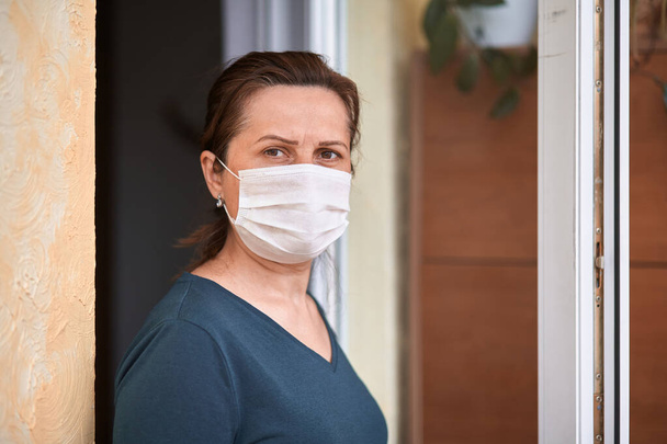Épidémie de coronavirus, quarantaine à domicile pendant l'infection à COVID-19. Femme inquiète dans un masque médical debout dans la porte ouverte
 - Photo, image