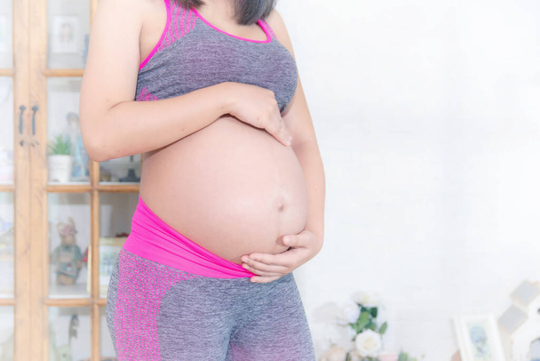 Közelkép terhes nő megérinti a nagy hasát, rózsaszín gyakorló ruhát visel. - Fotó, kép