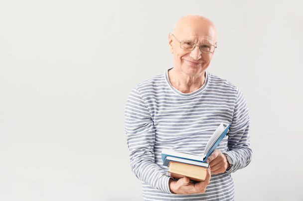 Portrait of elderly man with books on grey background - Фото, зображення