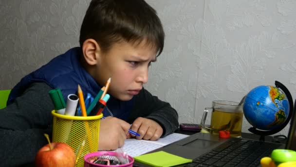 Fernstudium. Funny schoolboy bekommt Online-Bildung und macht während der Quarantäne Hausaufgaben mit Notizbuch. Er macht Grimassen und albert herum. Porträt aus nächster Nähe. - Filmmaterial, Video