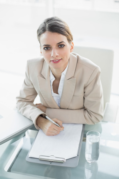 Softly smiling businesswoman writing on a clipboard looking at camera - Foto, Imagem