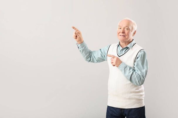 Portrait of elderly man showing something on grey background - Фото, изображение