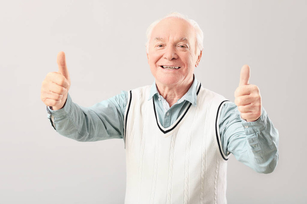 Portrait of elderly man showing thumb-up gesture on grey background - Photo, image