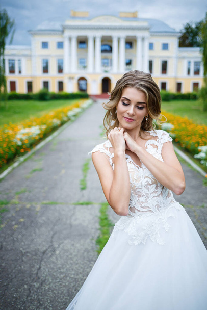 hermosa novia chica en un vestido blanco con un tren caminando sobre el fondo de una casa grande con columnas en el día de su boda
 - Foto, imagen