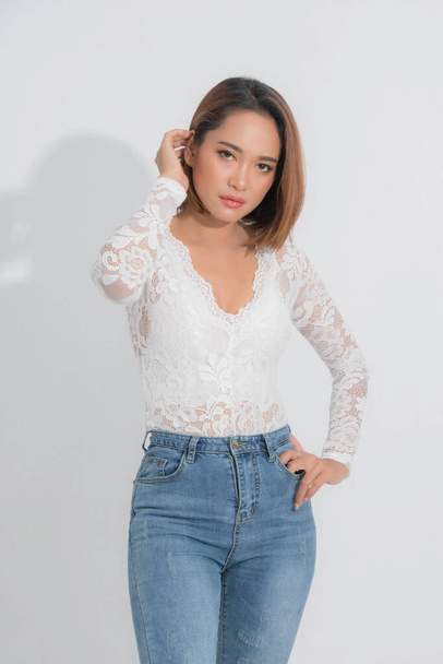 Beautiful portrait asian woman brown short bob wearing a white lace bodysuit and blue jeans in stand position with fashion on isolated white background. - Photo, Image