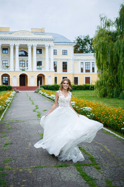 красива дівчина наречена в білій сукні з потягом і прогулянкою, повернутою на тлі великого будинку з колонами на день весілля
 - Фото, зображення
