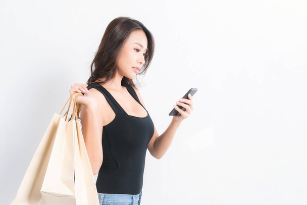 Happy beautiful asian woman black long-haired woman wearing a black shirt, jeans using a mobile phone and carrying shopping bags  on isolated gray background, Shopping summer sale concept. - Φωτογραφία, εικόνα
