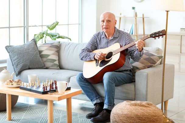 Oudere man speelt thuis gitaar - Foto, afbeelding