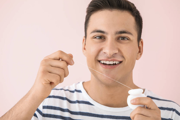 Handsome man flossing teeth on color background - Photo, Image