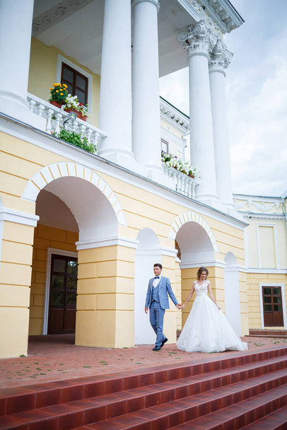 Νέος κομψός τύπος με το κοστούμι του γαμπρού και της νύφης όμορφο κορίτσι σε ένα λευκό φόρεμα με ένα τρένο με τα πόδια στο πάρκο την ημέρα του γάμου τους - Φωτογραφία, εικόνα