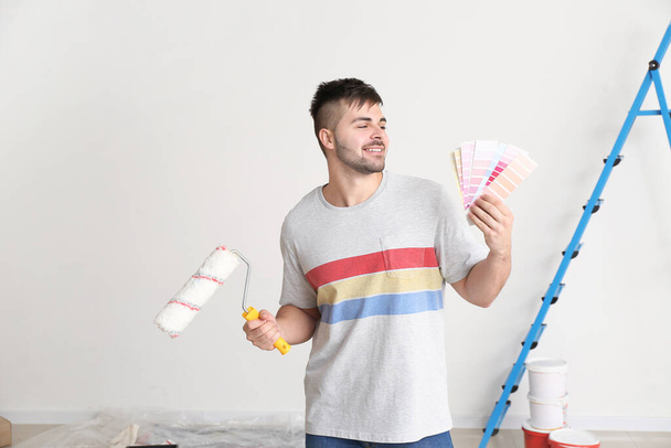 Молодой человек с цветными образцами и ролик краски в помещении
 - Фото, изображение