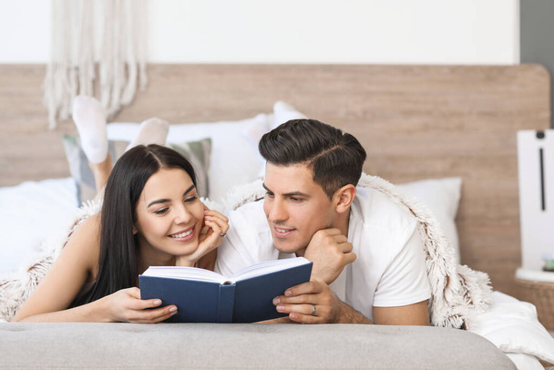 Happy young couple reading book in bedroom - Foto, imagen