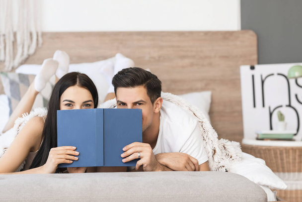 幸せな若いカップル読書本でベッドルーム - 写真・画像