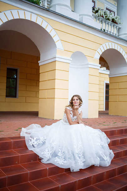 красива дівчина наречена в білій сукні з поїздом, що йде на тлі великого будинку з колонами на день весілля
 - Фото, зображення