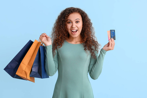 Jonge vrouw met creditcards en boodschappentassen op kleur achtergrond - Foto, afbeelding