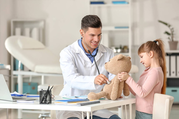 Pediatrician with toy showing little girl how to use stethoscope in clinic - Fotoğraf, Görsel