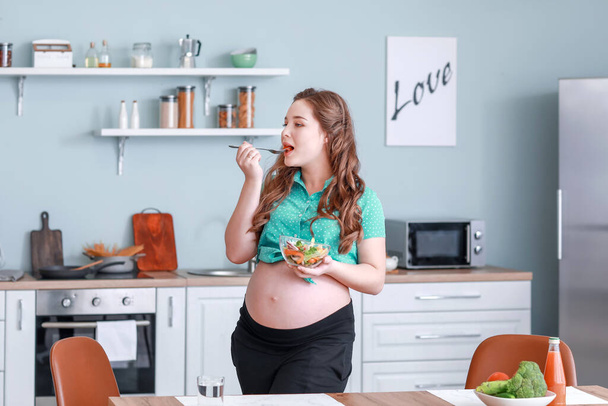 Kaunis raskaana oleva nainen terveellä salaatilla keittiössä
 - Valokuva, kuva