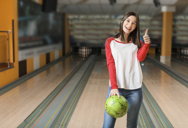 Mladá žena s kuličkou ukazující palec nahoru v bowlingovém klubu - Fotografie, Obrázek