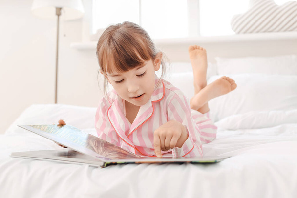 Söpö pieni tyttö lukee iltasatua kotona
 - Valokuva, kuva