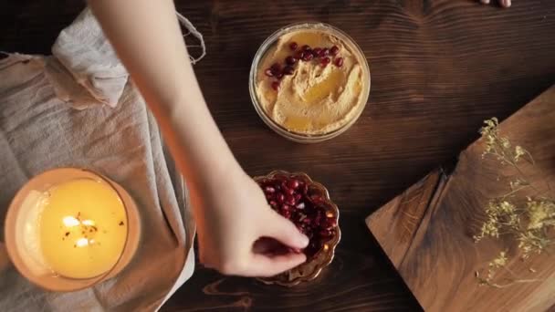 A young girl spreads pomegranate seeds on a homemade hummus in a bowl for decoration. Close-up. View from above - Video, Çekim