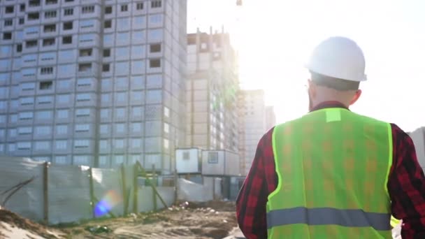 Following Shot of Professional Worker Wearing Hard Hat Holds blueprint, Walking Through Modern construction site - Séquence, vidéo