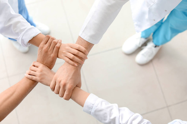 Group of doctors holding hands together in clinic, top view. Unity concept - Zdjęcie, obraz