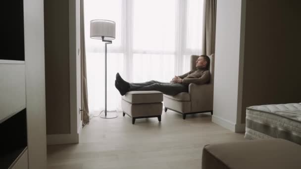 Muž středního věku leží na židli a zamyšleně se dívá z okna..  - Záběry, video