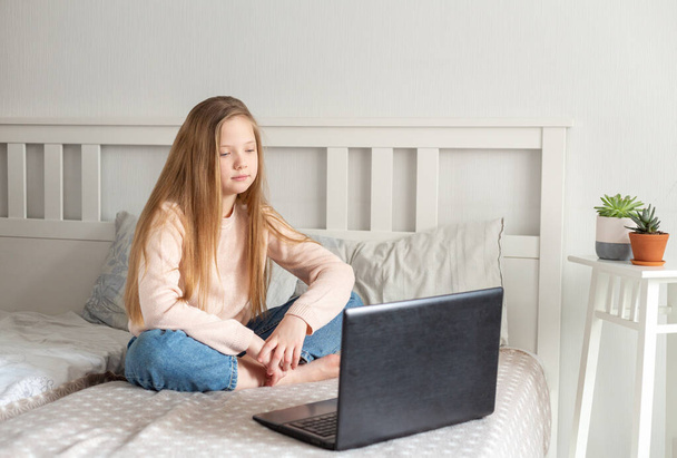 Schoolgirl with long hair using laptop computer at home. Distance learning, online education, home education, quarantine concept. - 写真・画像